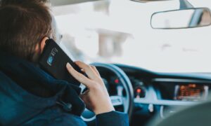man sitting on car seat front of steering wheel holding phone